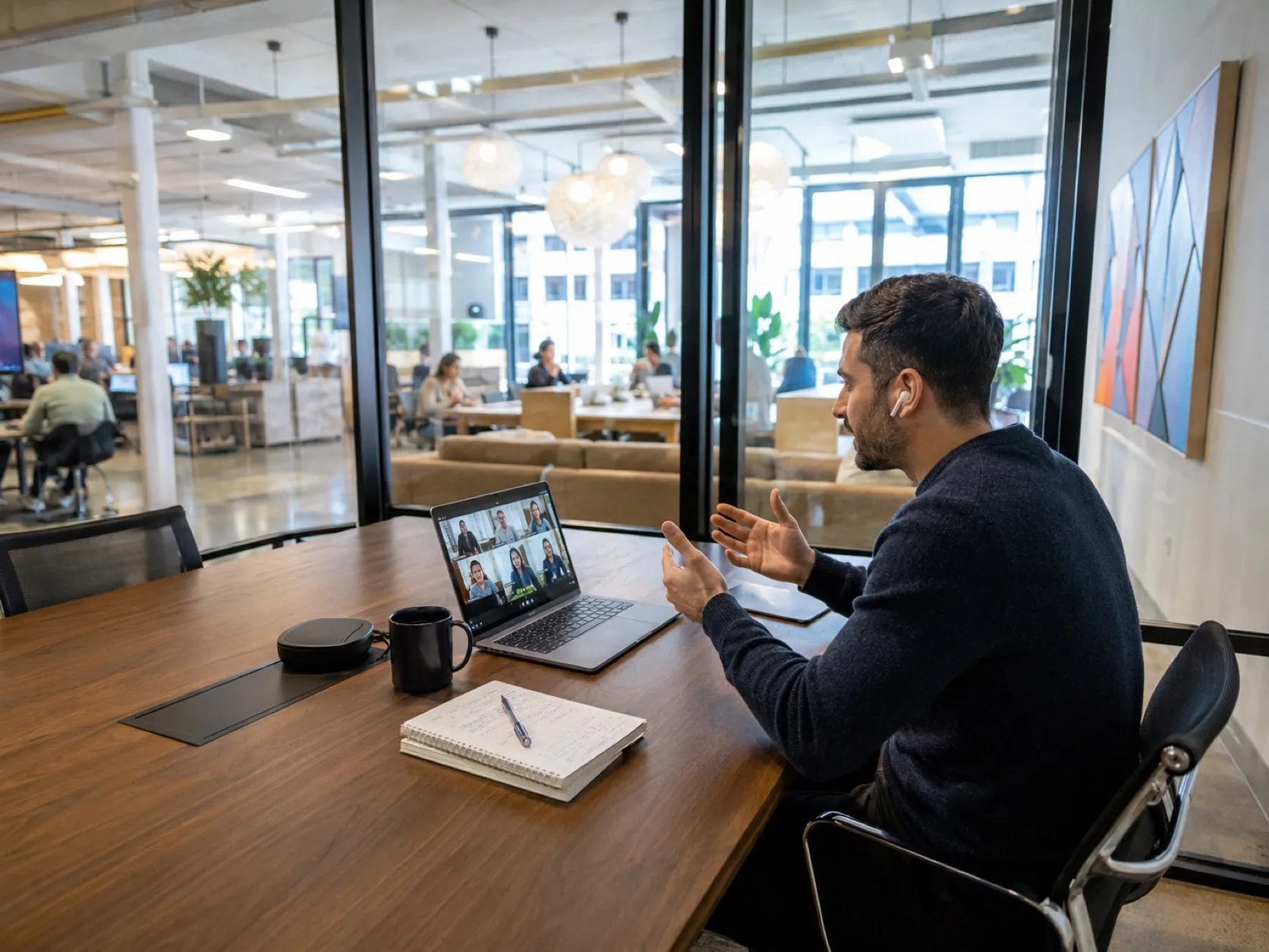 A glass meeting room mid video call, one member presenting to a laptop, the floor visible behind.